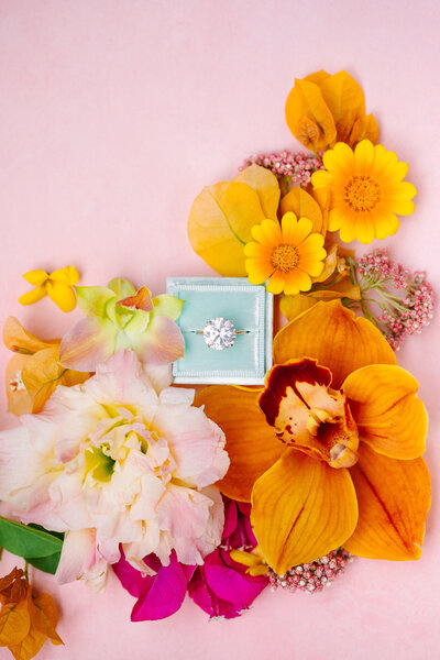ring box with solitaire ring surrounded by flowers in a flat lay