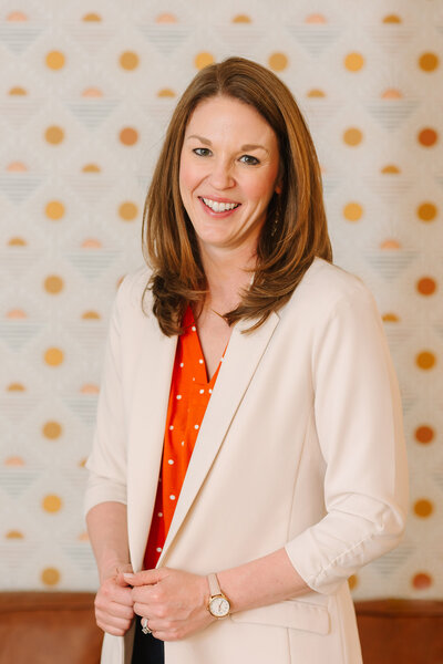 Lindsay smiling in front of a wall with playful wallpaper 