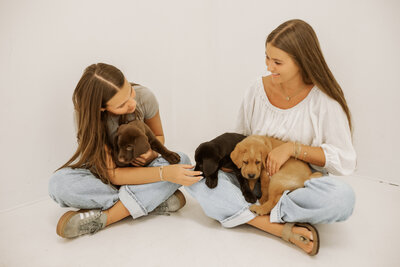 Two girls holding labrador retriever puppies