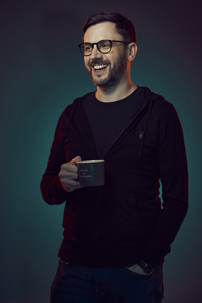 Creative portrait of Mike Ball in a dark setting, wearing glasses and a relaxed outfit, exuding a confident and modern vibe, captured by Ylva Erevall.