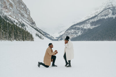 Man on one knee on frozen Lake Louise proposing to his girlfriend