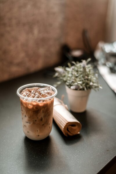 A cup of iced coffee on a table near a green plant.