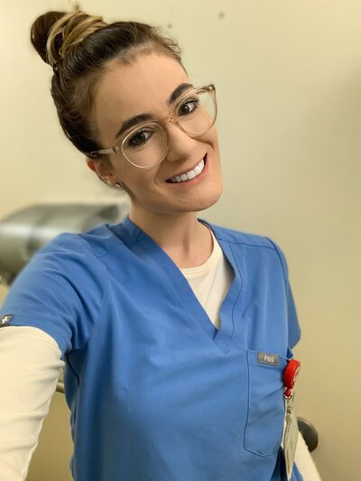 Madison in blue medical scrubs smiling warmly, captured during her pre-health post-bacc journey and time working in the ED in NYC.