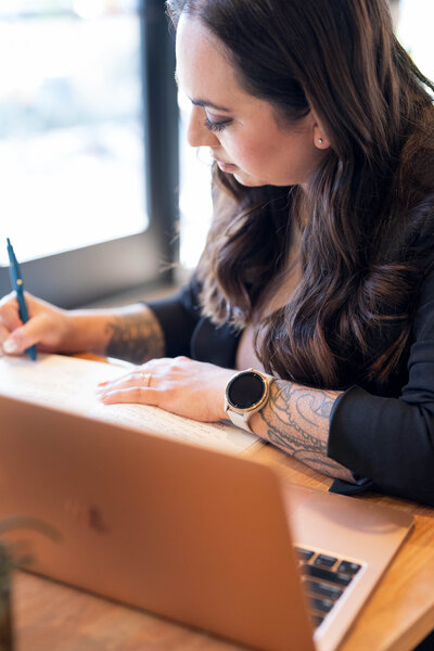 Stephanie, Founder of BCWise Consulting sitting at a desk on her computer writing a note
