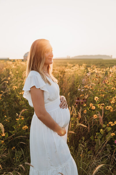 Pregnant Mother holds her baby bum in a flower field at sunset.