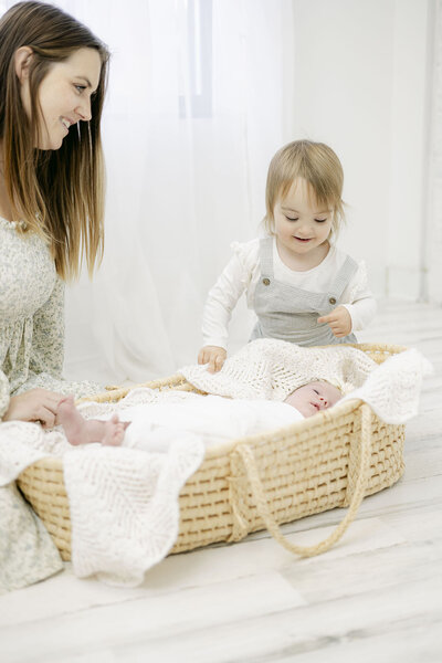 Mother and toddler girl looking at newborn baby during newborn photography session.