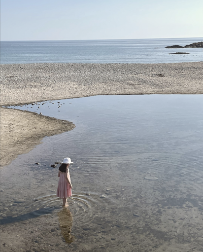 Daughter stading in the shallow beach water in sundress and hat.