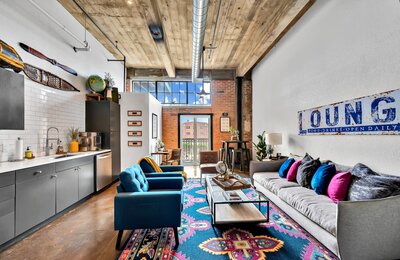 Living room and kitchen with exposed brick and pipe in this two-bedroom, two-bathroom vacation rental condo in the historic Behrens building in downtown Waco, TX just blocks from the Silos, Baylor University, and Spice Street.