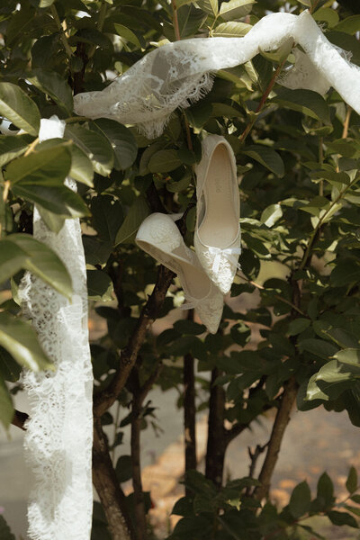 Wedding details of bridal shoes and lace hanging from a tree