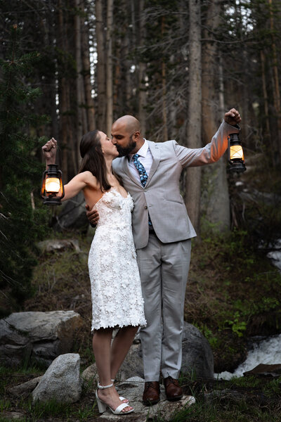 A couple kisses in a forest while holding lanterns in the air