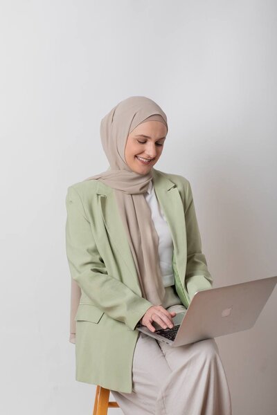 Client Zey smiling while working on her laptop after joining Ayah’s mentorship program, celebrating new business wins and growth.