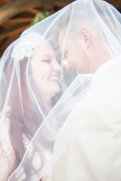 A happy couple shares a moment laughing together underneath the bride's veil during their gorgeous garden wedding.