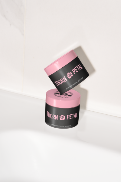 Stacked body lotion containers that are black with pink lids that read Thorn and Petal in front of a white background