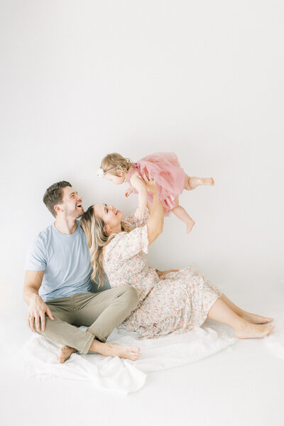 Mom and dad holding baby up in the air while smiling for their daughters one year birthday photo session