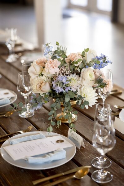 Floral arrangement with white, pink and blue flowers on a laid wooden table