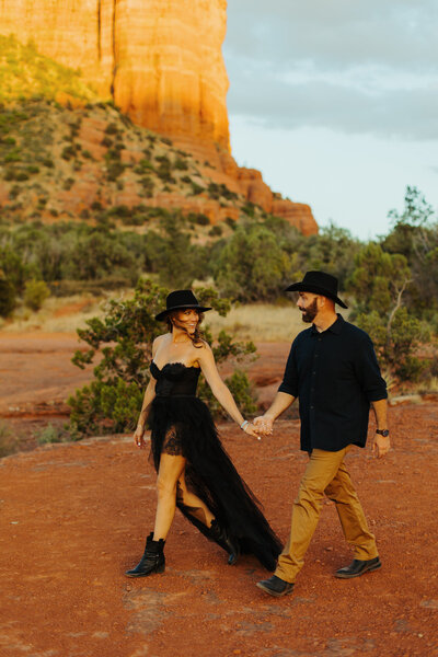 man and woman in western attire walking in sedona landscape