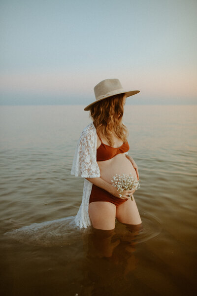Maternity Photographer, an expectant pregnant mom-to-be stands in ocean waters holding her belly fondly