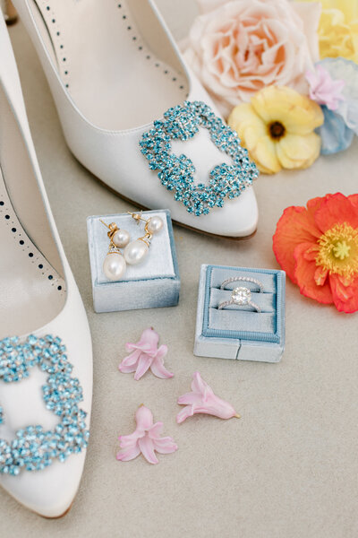 Flat lay of wedding rings, white and blue wedding shoes, and colorful flowers