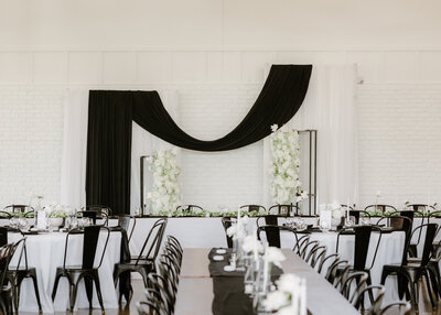 Interior of the August House venue in Dickinson, North Dakota, showing a spacious white-walled wedding reception hall with high ceilings, large windows, minimalist decor, and modern chandelier lighting.