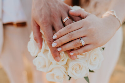 Two hands are on top of a bouquet showing the wedding rings