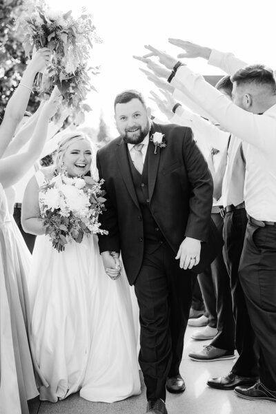black and white photo of bride and groom walking through wedding party line