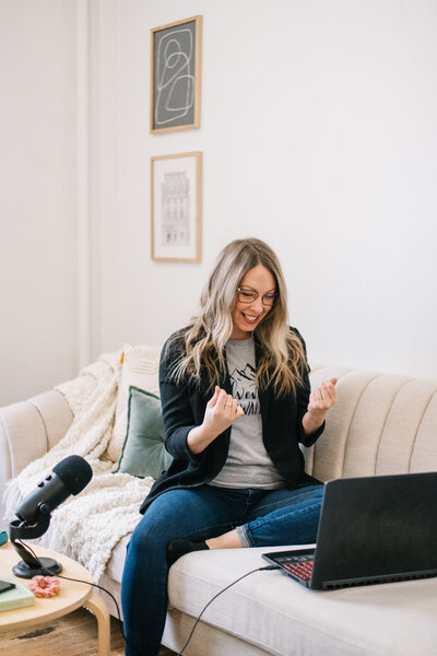 Sammy sitting on a couch with her laptop and a microphone on the coffee table next to her