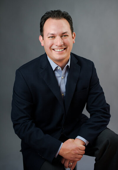 Headshot photo of a handsome business man in dark blue suit smiling.