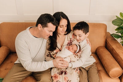A family of four, smiling at their newborn baby girl at their baby photo session