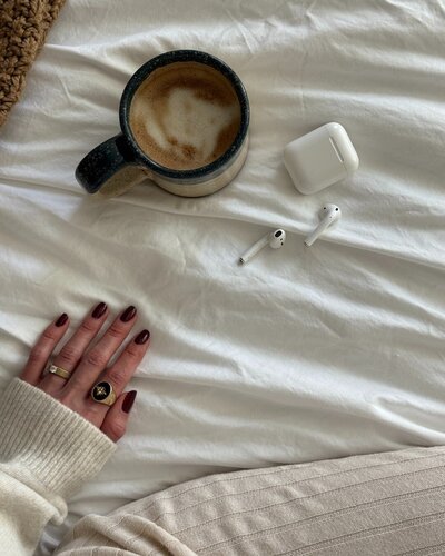female influencer virtual assistant sitting on her bed drinking coffee and listening to airpods