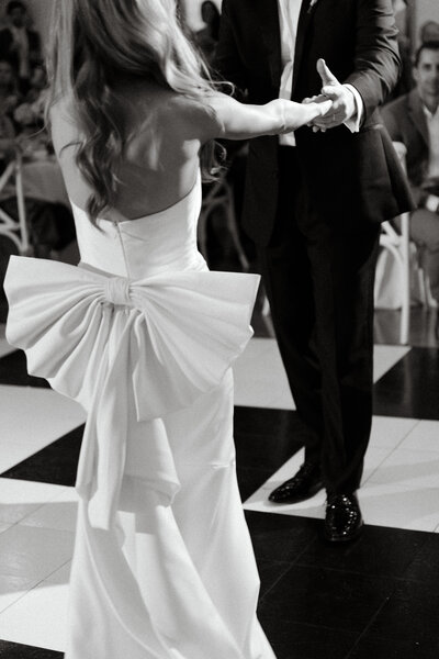 Blair and Travis share a joyful first dance at their wedding reception, with the bride’s statement bow dress flowing as they move across a black-and-white checkered dance floor.