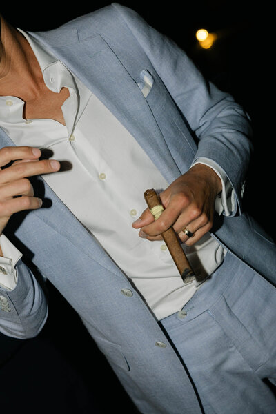 Groom in a light blue tailored suit holds a cigar during his wedding reception at The Paseo Wedding Venue. 