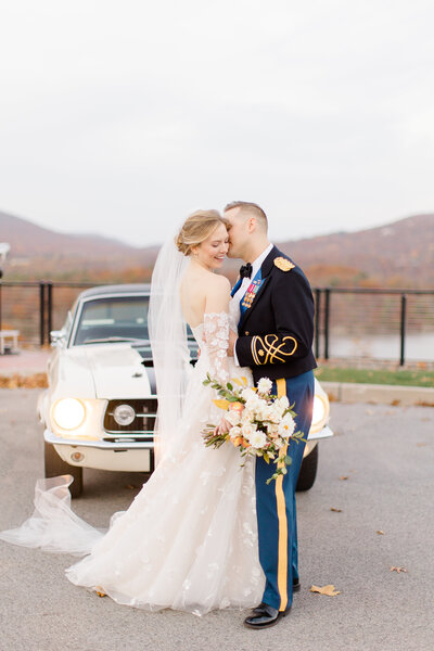 Bride and groom in military uniform posing in front of a vintage car