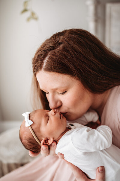 mom holding baby girl facing outward and kissing her face