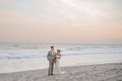 A bride and groom hold hands on a beach on the coast of NC on their wedding day.