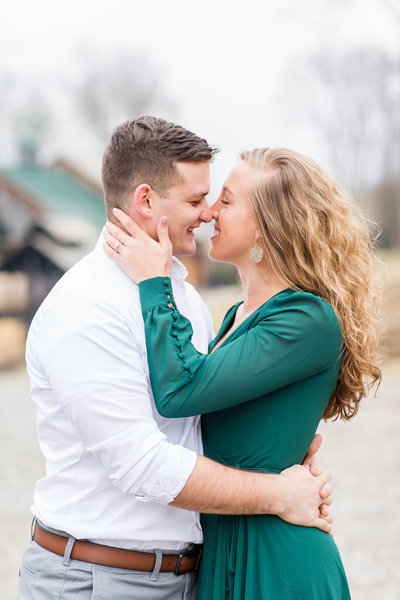Bride in a green dress touching her nose to her fiance at their winter engagement photos at Rivercrest Farm photographed by akron ohio wedding photographer