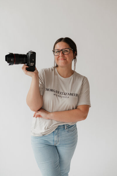A photographer with one arm across her chest and the other holding up a camera 