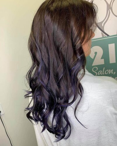 A woman with long, dark hair featuring subtle blue highlights, showcasing a stylish and unique hairstyle created by 212 Salon, Spa, & Barbershop.