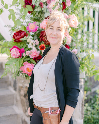 Carmel smiling in front of a lush pillar of pink and deep red flowers at Stonehaven.