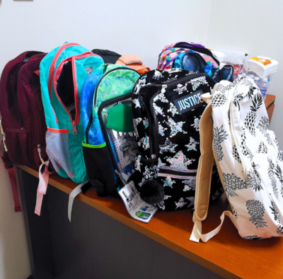 9 backpacks sit in a row on a tabletop from a bookbag donation drive.