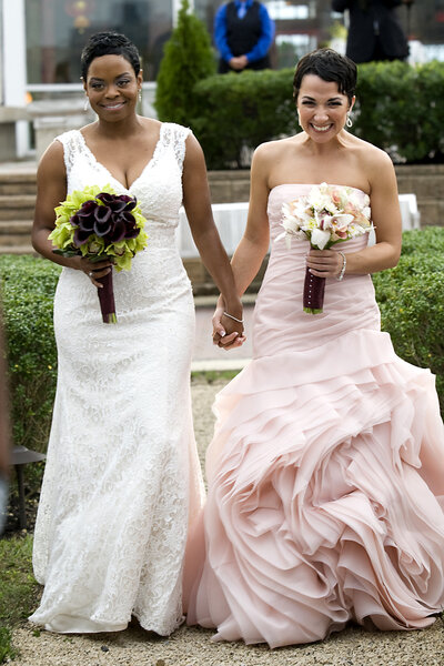 A wedding couple holding hands and walking together as they both hold bouquets of flowers 