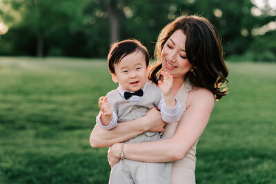 A korean mama holding up her son dressed in a suit and clapping his hands