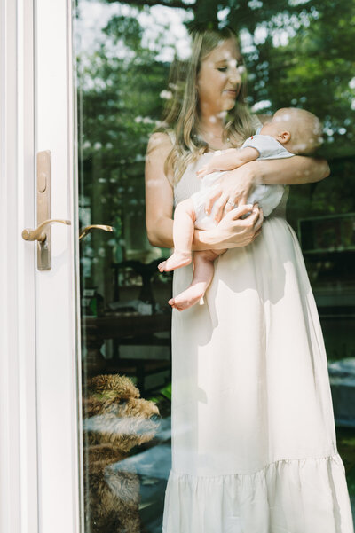 photo of mom holding baby with dog taken through glass door