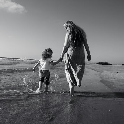 Mother holding child’s hand while walking on the beach, representing Golden Mamas motherhood community