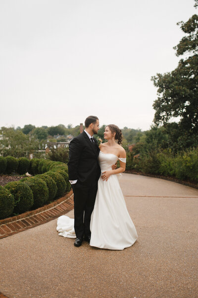 Couple in wedding attire poses in English looking garden on a cloudy day.