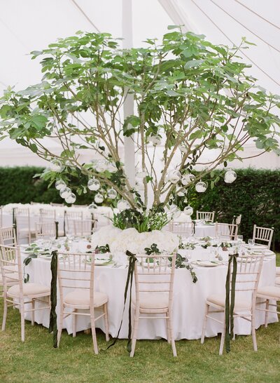 A large display of long stemmed foliage placed on a table with hanging globes of candles