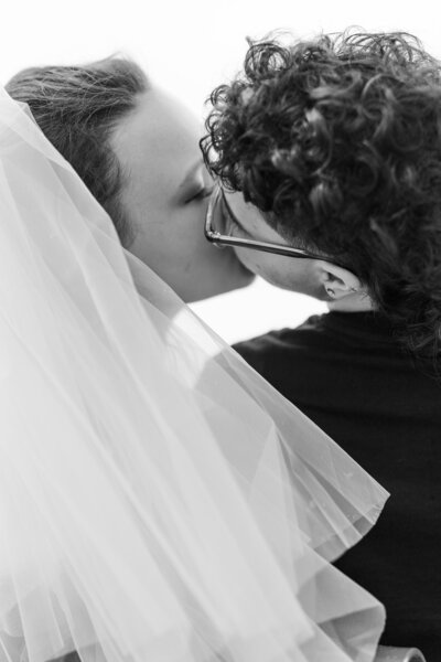 black and white image of bride and groom sharing a kiss, hidden under a veil