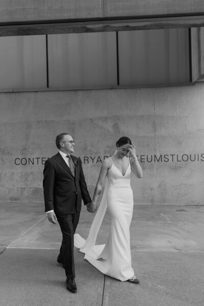 Black and white image of bride and groom walking outside of Contemporary Art Museum in Missouri