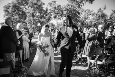 An Austin-based wedding photographer captures a black and white photo of a bride and groom walking down the aisle.