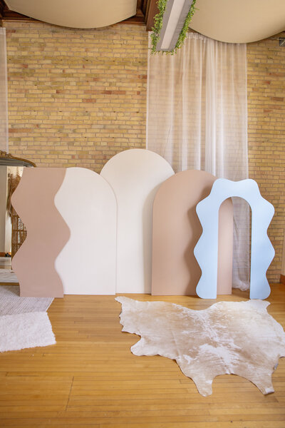 Five wooden backdrops set up overlapping. One brown wavy, two white arches, one brown arch, and one blue wavy arch.