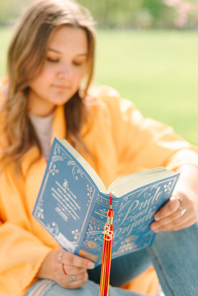 High school senior girl reading a book and using her tassel as a bookmark